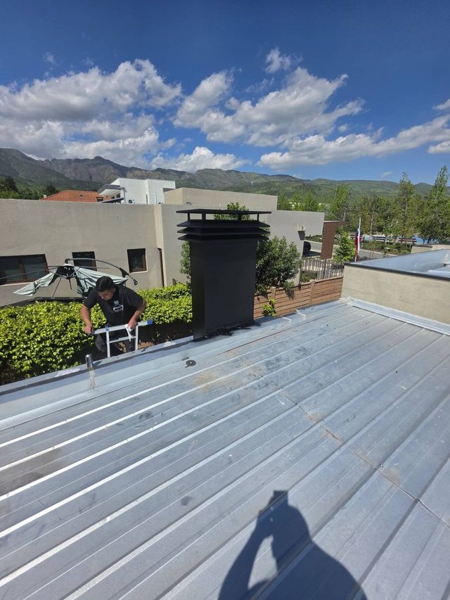 Instalador fijando el sombrerete de la campana en el techo, con cerros al fondo