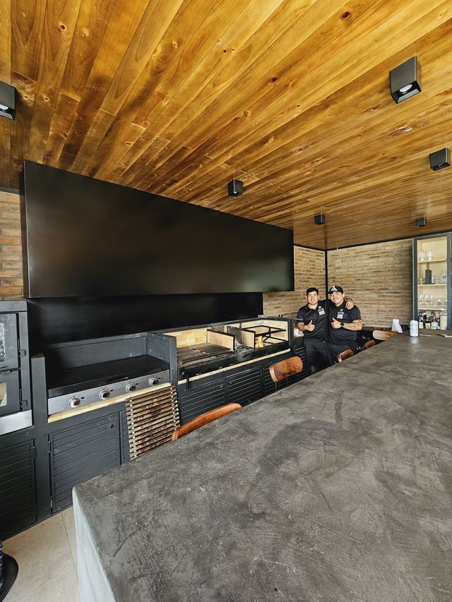 Campana rectangular negra sobre las parrillas de un quincho con techo de madera