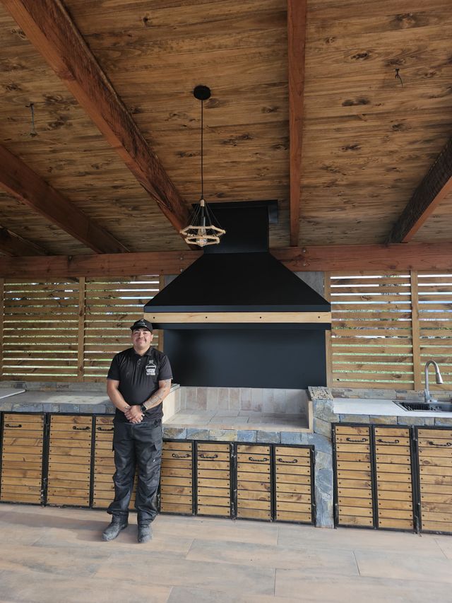 Instalador bajo una campana piramidal negra, en un quincho con muebles de madera