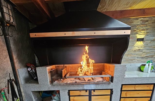 Campana con encaje de madera sobre fogón con fuego y muro de piedra
