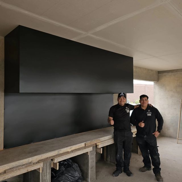 Dos instaladores bajo una campana rectangular colgante, sobre mesón de hormigón