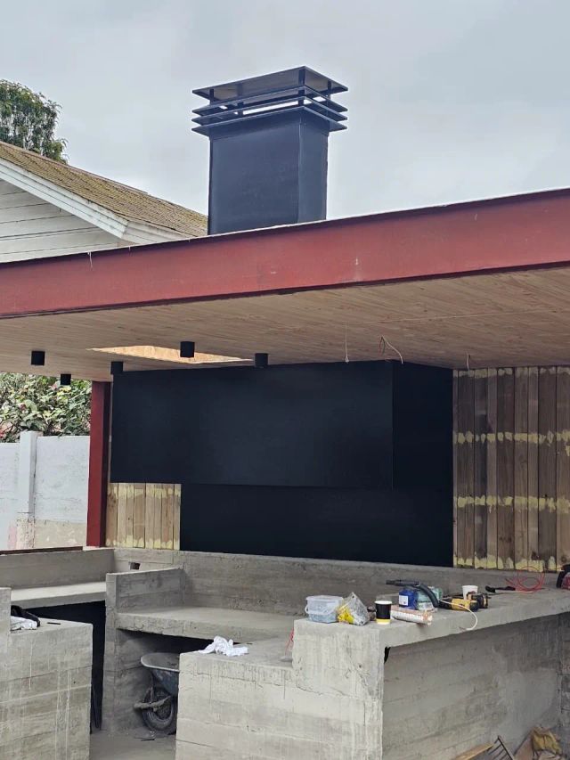 Quincho exterior con campana negra y chimenea sobre el techo