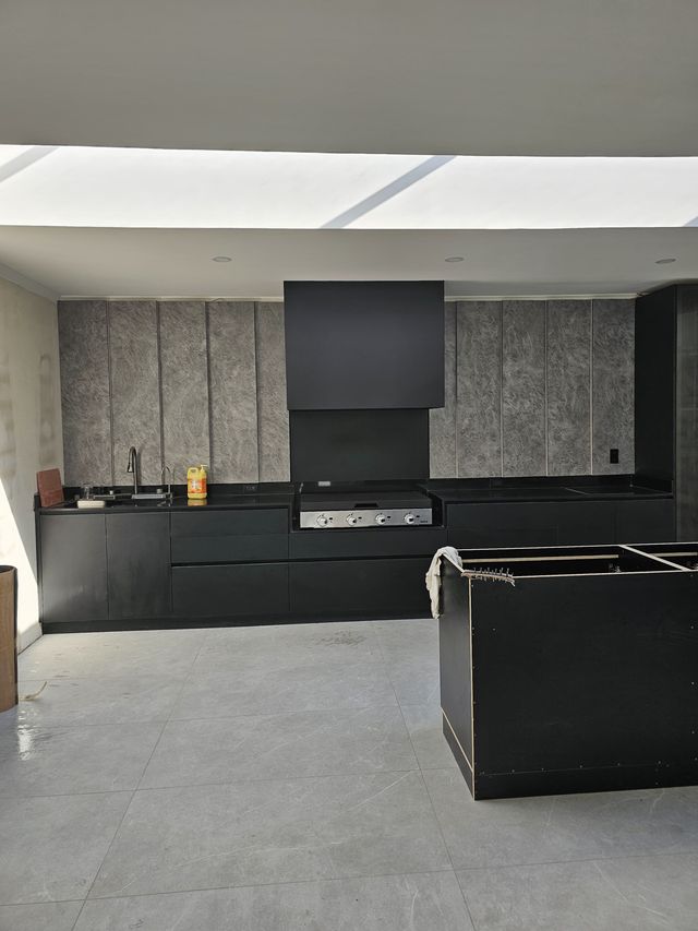 Campana rectangular negra sobre una cocina exterior con muebles negros