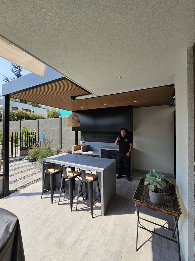 Terraza con comedor exterior y quincho con campana negra al fondo
