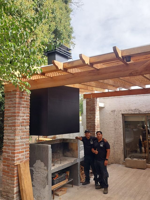 Dos instaladores bajo una pérgola con muro de ladrillo y campana rectangular