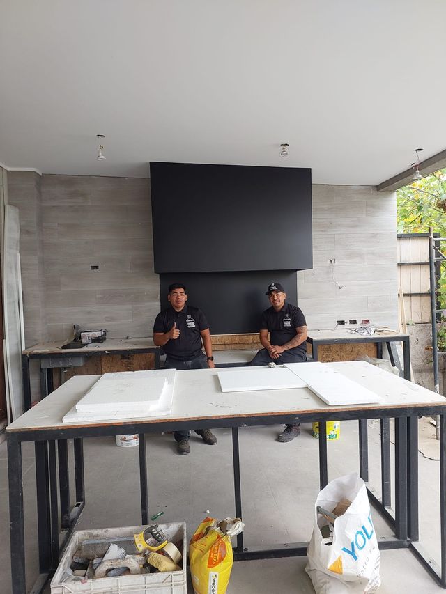 Dos instaladores bajo una campana rectangular, junto al mesón en obra