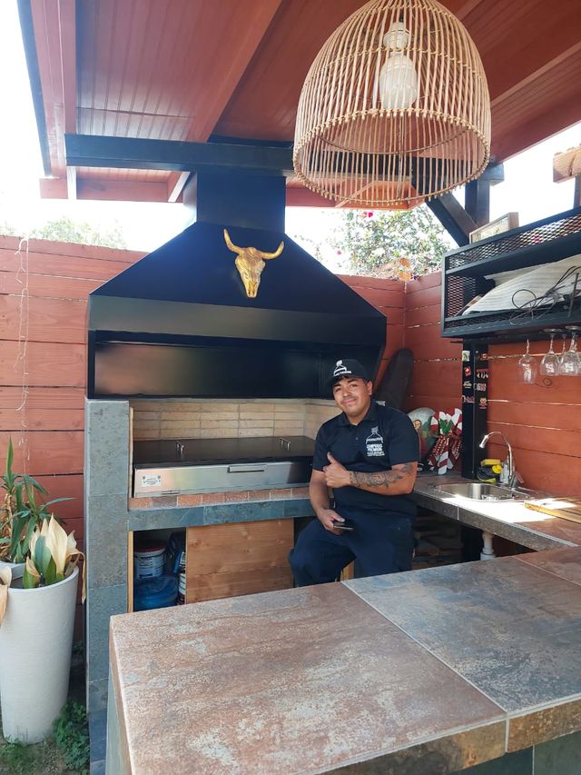 Instalador junto a una campana piramidal sobre fogón, en un quincho decorado