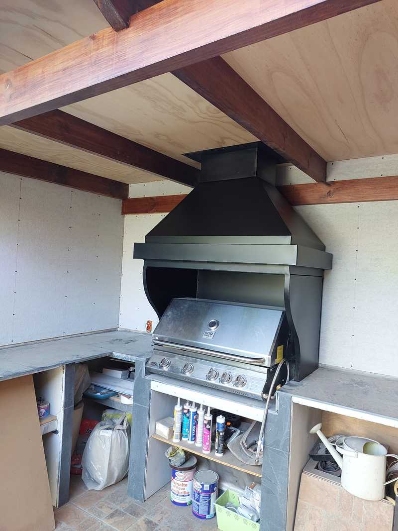 Campana con cinturón sobre parrilla a gas en quincho bajo techo