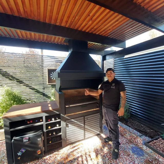 Instalador junto a una campana piramidal sobre parrilla, en un quincho exterior