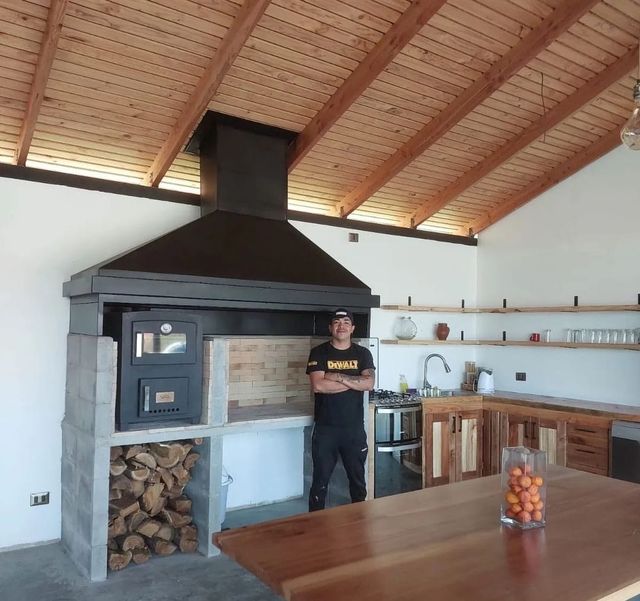 Campana piramidal sobre horno y leñera, en un quincho con techo de madera