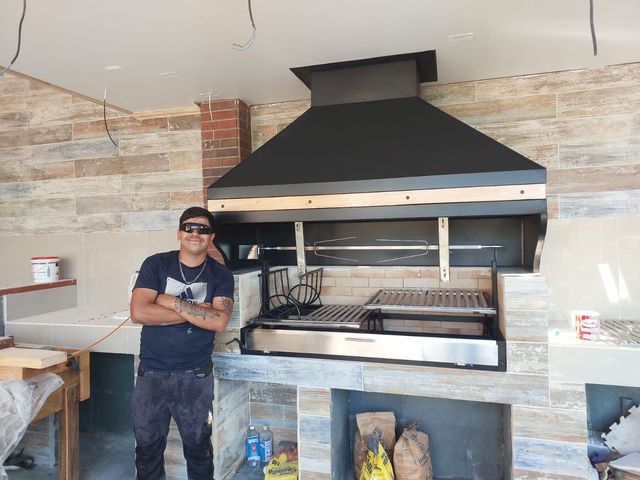 Instalador junto a una campana piramidal con franja de madera y parrilla de acero