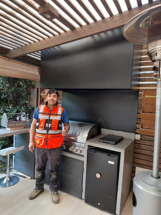 Instalador junto a una campana rectangular, muebles negros y parrilla a gas