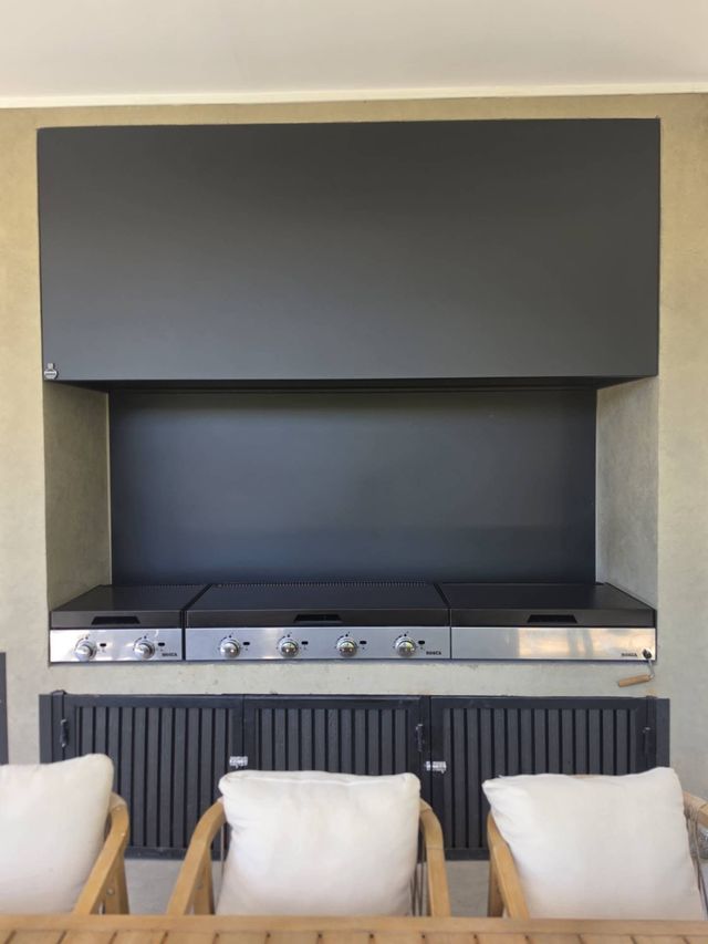 Campana negra de gran formato sobre parrillas a gas y muebles negros, en un quincho de Chicureo