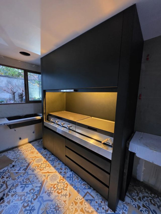 Quincho modular negro con iluminación interior, parrillas de acero y mueble con cajones